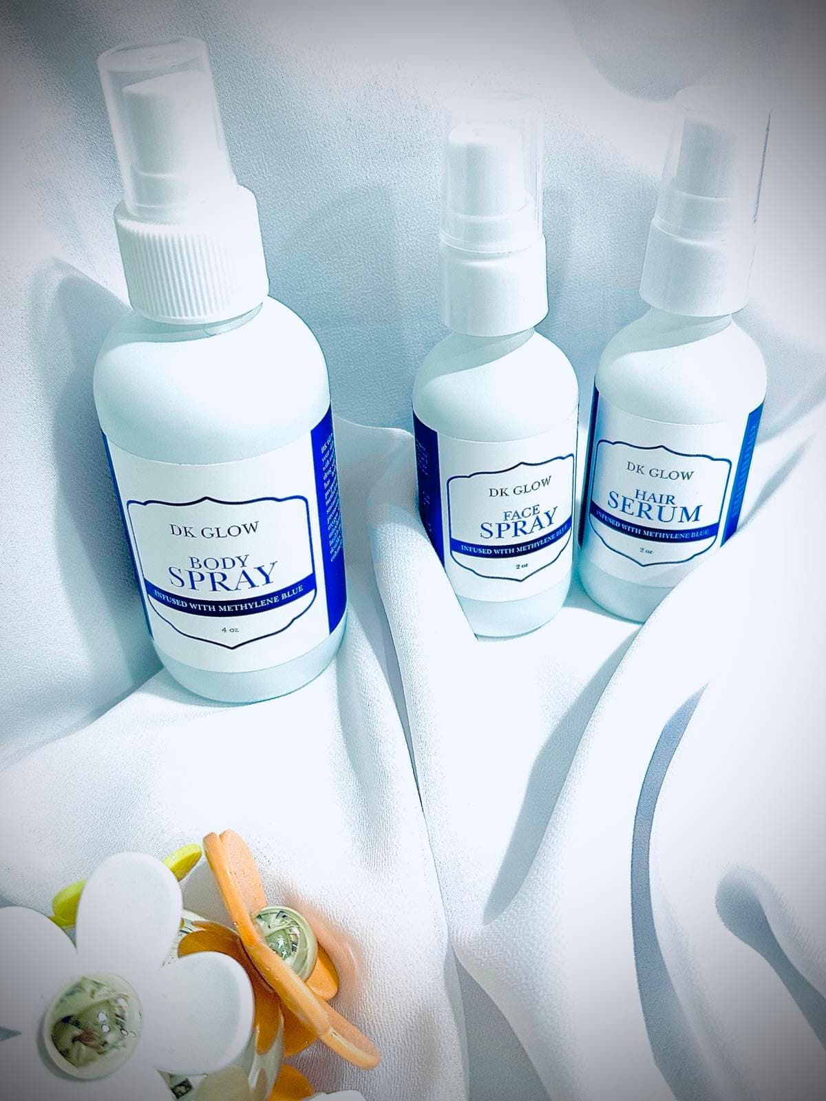 DKGlow Methylene Blue Body Spray, Face Spray, and Hair Serum bottles staged on white fabric